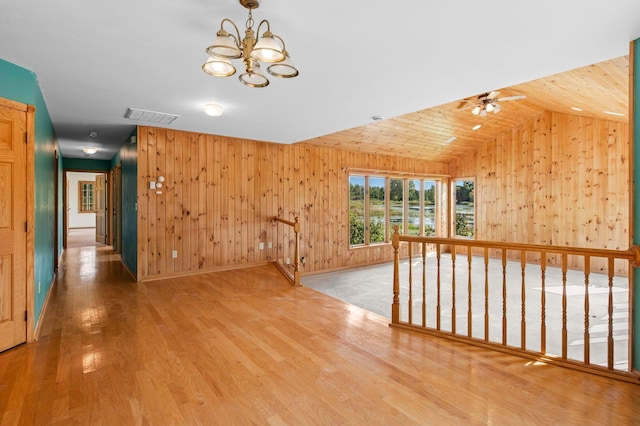 unfurnished room with lofted ceiling, ceiling fan with notable chandelier, wooden walls, and hardwood / wood-style flooring