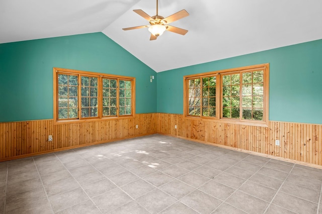 tiled empty room with vaulted ceiling, ceiling fan, and wooden walls