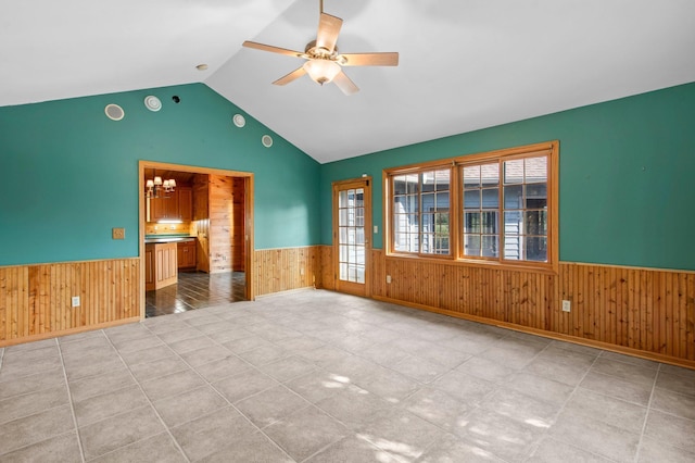 tiled spare room featuring ceiling fan with notable chandelier, vaulted ceiling, and wooden walls