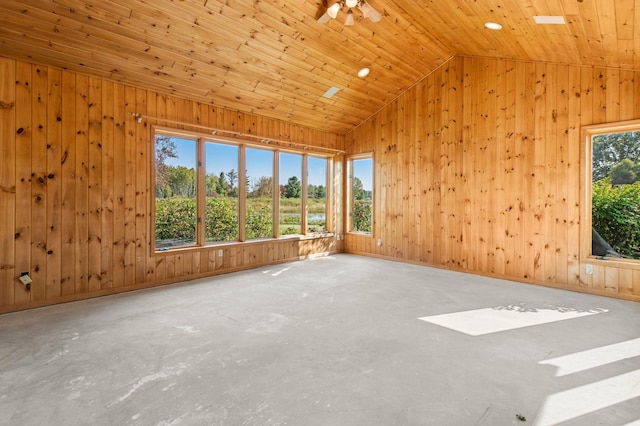 empty room featuring concrete flooring, ceiling fan, wooden walls, and vaulted ceiling