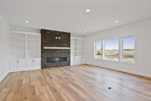 unfurnished living room with built in shelves, a fireplace, and light hardwood / wood-style floors