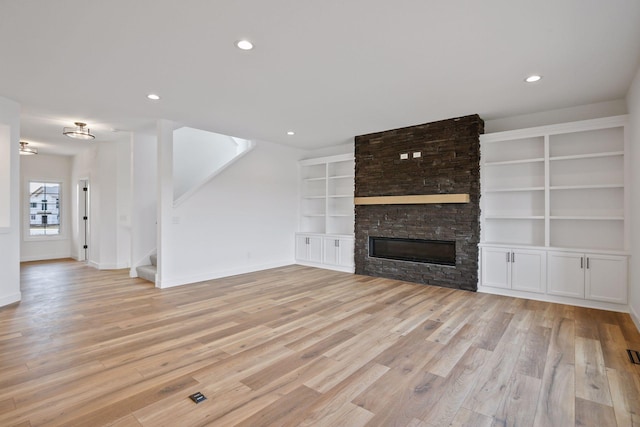 unfurnished living room featuring a fireplace, built in shelves, and light wood-type flooring