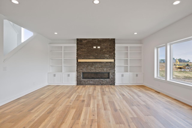 unfurnished living room with a fireplace, built in features, and light wood-type flooring