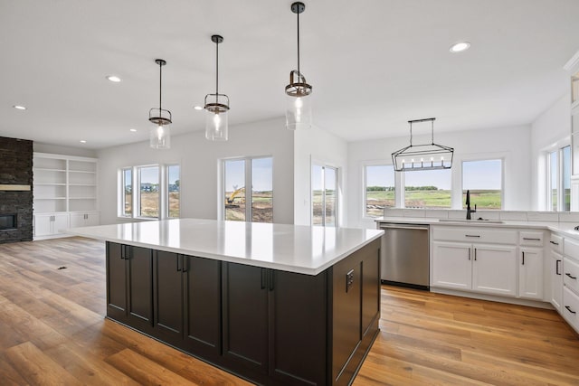 kitchen featuring a center island, a stone fireplace, sink, stainless steel dishwasher, and decorative light fixtures