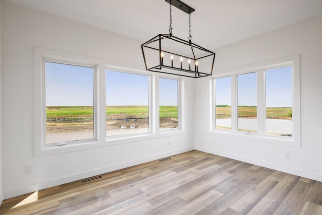 unfurnished dining area with a chandelier and light wood-type flooring