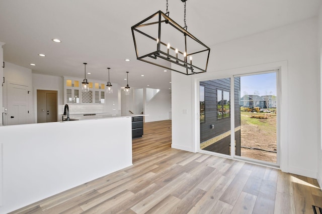 kitchen with sink, decorative light fixtures, an inviting chandelier, light hardwood / wood-style floors, and white cabinetry