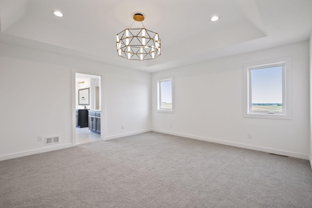 carpeted spare room featuring a raised ceiling and a notable chandelier