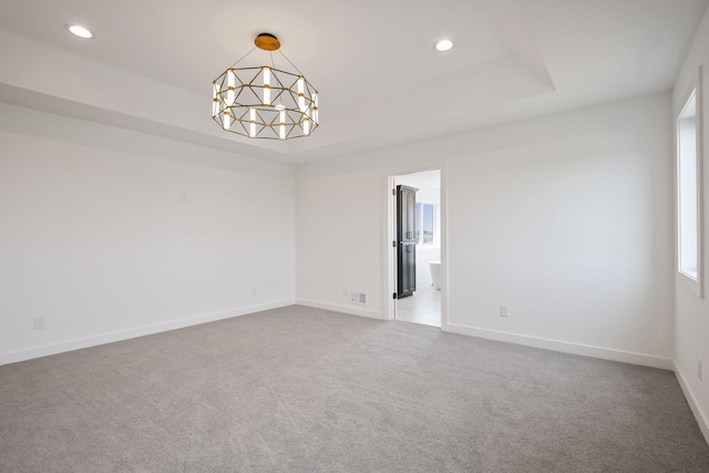 carpeted empty room with a raised ceiling and a chandelier