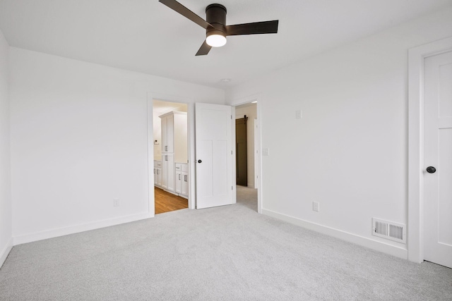 unfurnished bedroom with ceiling fan, ensuite bathroom, and light carpet