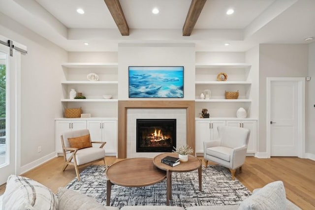 living area with a barn door, built in features, beamed ceiling, and light hardwood / wood-style floors