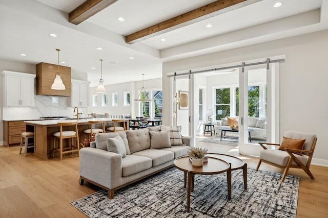 living room featuring light wood-type flooring, beam ceiling, and a barn door