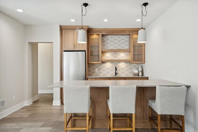 kitchen featuring decorative light fixtures, stainless steel fridge, light hardwood / wood-style floors, and a breakfast bar