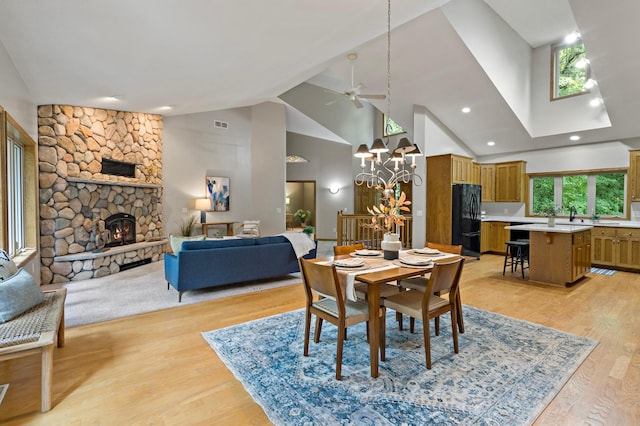 dining room with ceiling fan with notable chandelier, a fireplace, plenty of natural light, and light hardwood / wood-style flooring