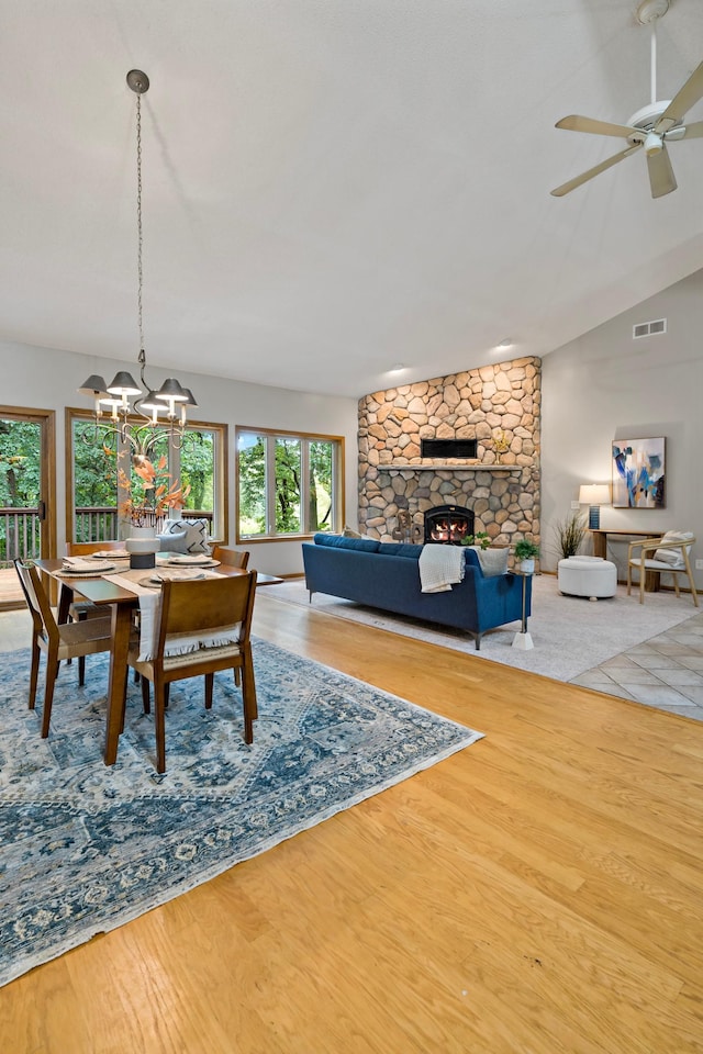 dining space featuring ceiling fan with notable chandelier, hardwood / wood-style floors, vaulted ceiling, and a fireplace