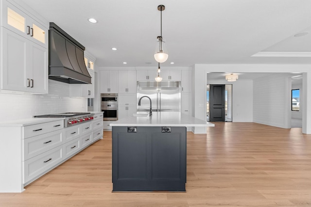 kitchen featuring appliances with stainless steel finishes, custom range hood, an island with sink, and white cabinets