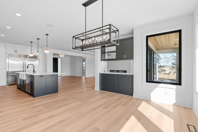 kitchen featuring light wood-type flooring, pendant lighting, appliances with stainless steel finishes, and a center island with sink