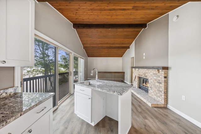 kitchen with light stone countertops, sink, vaulted ceiling with beams, wood ceiling, and light hardwood / wood-style flooring