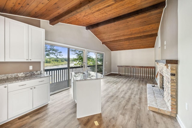 kitchen with light stone counters, white cabinetry, vaulted ceiling with beams, and a water view