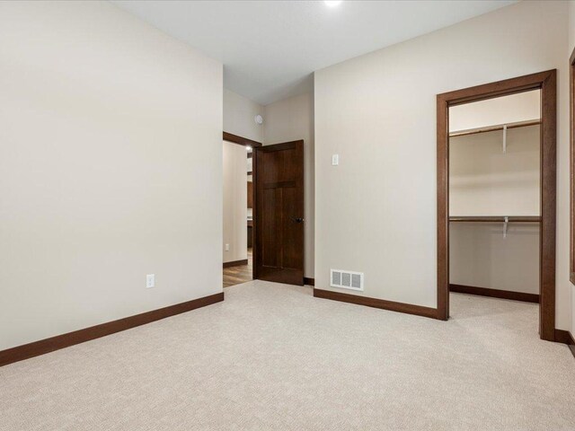 unfurnished bedroom with a walk in closet, light carpet, and a closet