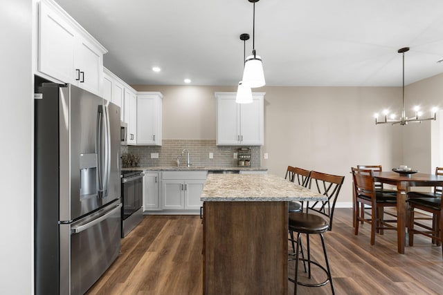 kitchen featuring appliances with stainless steel finishes, pendant lighting, a breakfast bar area, white cabinets, and dark wood-type flooring