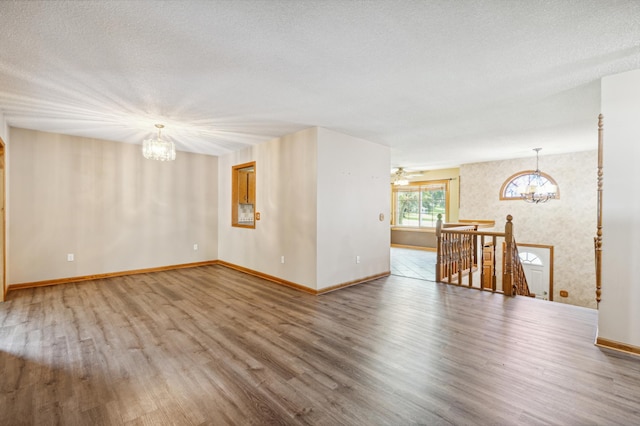 empty room with a textured ceiling, ceiling fan with notable chandelier, and hardwood / wood-style flooring