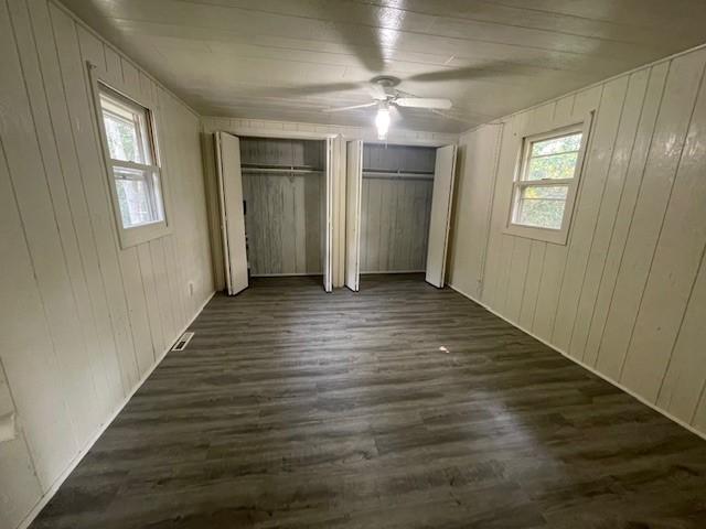 unfurnished bedroom featuring wood walls, ceiling fan, dark hardwood / wood-style floors, and multiple closets