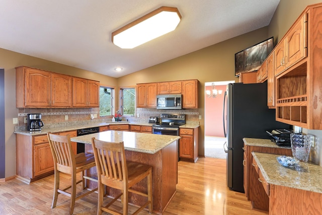 kitchen featuring a kitchen bar, appliances with stainless steel finishes, vaulted ceiling, light hardwood / wood-style flooring, and a kitchen island