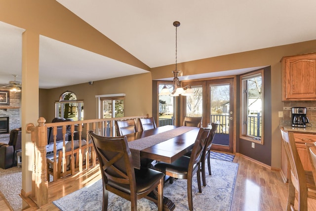 dining space featuring a fireplace, ceiling fan with notable chandelier, vaulted ceiling, and light wood-type flooring