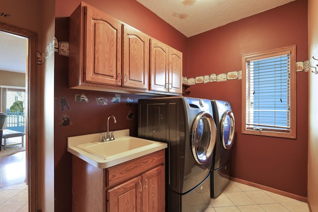 laundry area featuring cabinets, a textured ceiling, washer and clothes dryer, sink, and light tile patterned flooring