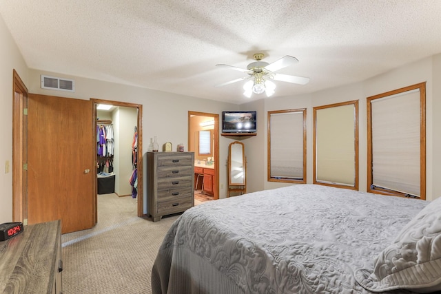 carpeted bedroom with a walk in closet, ensuite bathroom, a textured ceiling, ceiling fan, and a closet