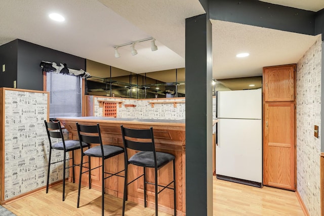 bar with a textured ceiling, rail lighting, white fridge, and light hardwood / wood-style flooring