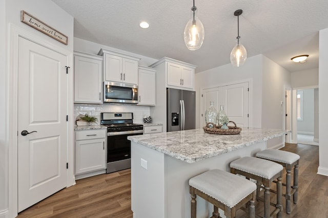 kitchen with appliances with stainless steel finishes, hardwood / wood-style flooring, a kitchen island, and white cabinetry