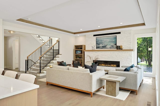 living room featuring a stone fireplace, a tray ceiling, and light hardwood / wood-style flooring