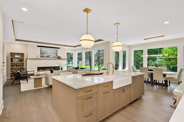 kitchen with light hardwood / wood-style floors, sink, light brown cabinets, decorative light fixtures, and a stone fireplace