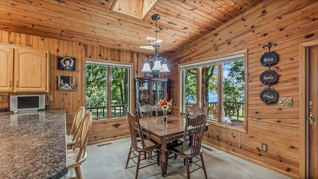 carpeted dining room with wood ceiling, wood walls, a skylight, and a notable chandelier