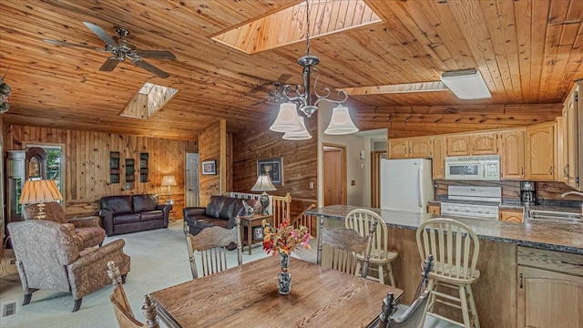 carpeted dining space with ceiling fan, vaulted ceiling with skylight, sink, wooden walls, and wooden ceiling