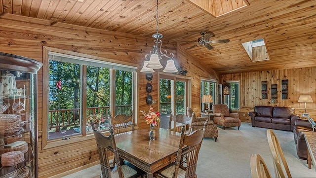 dining space featuring wood ceiling, vaulted ceiling with skylight, wood walls, and ceiling fan