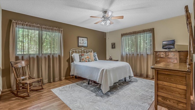 bedroom with multiple windows, a textured ceiling, ceiling fan, and light hardwood / wood-style flooring