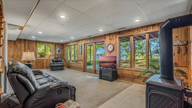 carpeted living room with a drop ceiling, a wood stove, and wooden walls