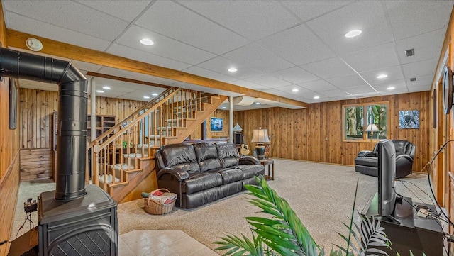 living room with carpet flooring, a drop ceiling, wooden walls, and a wood stove