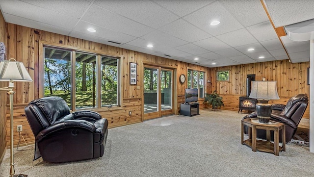 living room featuring wood walls, carpet flooring, and a paneled ceiling