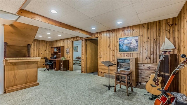 carpeted home office featuring wooden walls and a drop ceiling