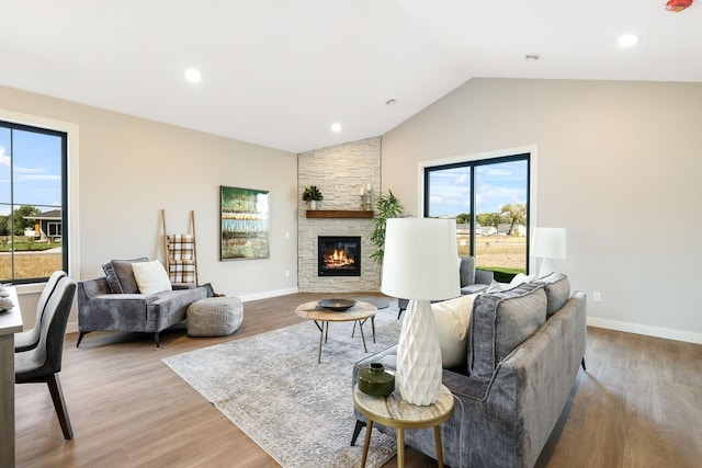 living room with vaulted ceiling, a stone fireplace, and light hardwood / wood-style floors