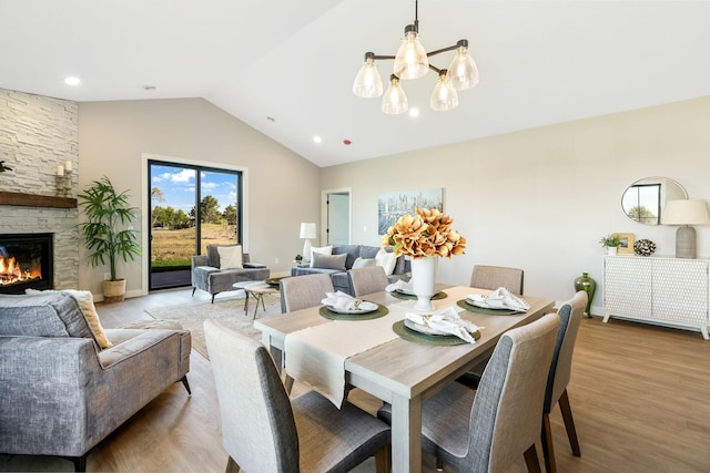 dining space with vaulted ceiling, a fireplace, an inviting chandelier, and light hardwood / wood-style flooring