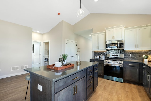 kitchen with vaulted ceiling, light hardwood / wood-style floors, washer / clothes dryer, stainless steel appliances, and white cabinets