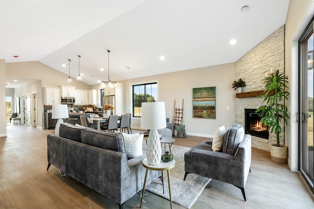 living room featuring a fireplace, vaulted ceiling, light hardwood / wood-style flooring, and an inviting chandelier