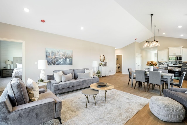 living room featuring lofted ceiling, washer / clothes dryer, a notable chandelier, and light hardwood / wood-style floors