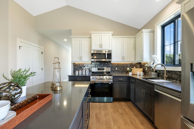 kitchen with vaulted ceiling, light hardwood / wood-style flooring, stainless steel appliances, sink, and white cabinets