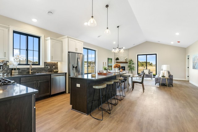 kitchen featuring a kitchen island, a fireplace, appliances with stainless steel finishes, a chandelier, and white cabinets