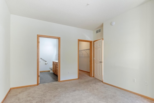 unfurnished bedroom with a closet, a textured ceiling, light colored carpet, a walk in closet, and ensuite bathroom